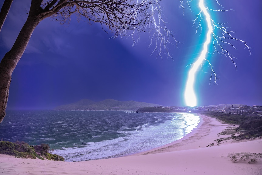 A bolt of lightning illuminates a beach as it strikes in the distance.