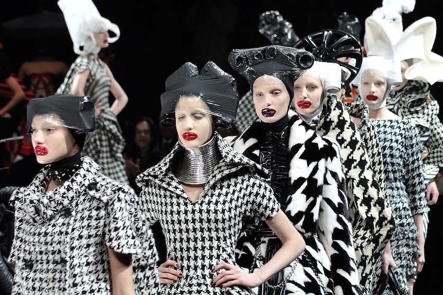 Models dressed in extravagant black-and-white tartan outfits and headpieces walk down a catwalk
