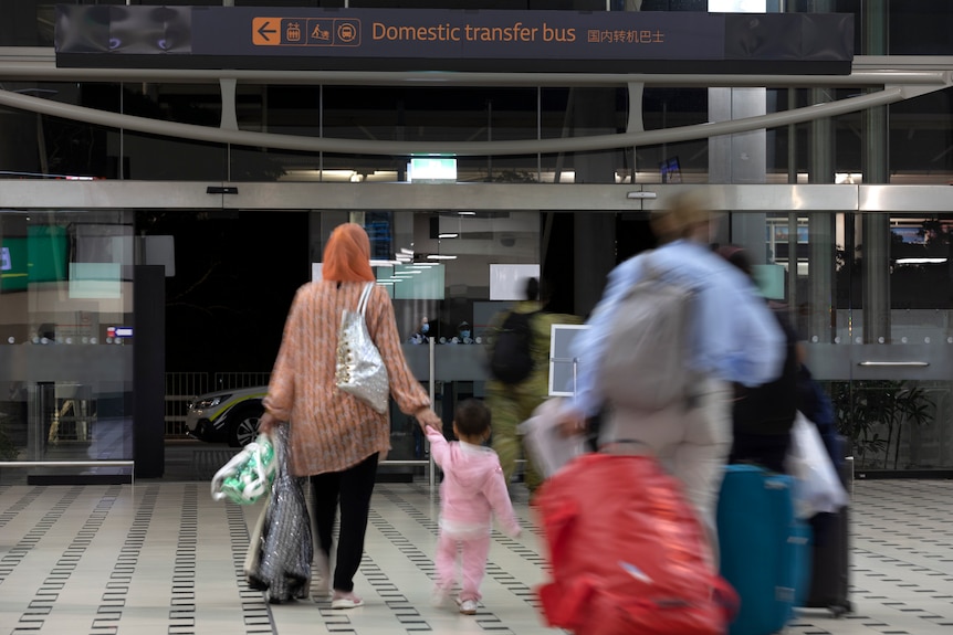 A family carrying luggage walks out the doors of an airport terminal