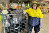 a woman in high-vis workwear standing next to a crate full of old computers and TVs