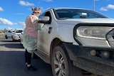 A woman in protective clothing speaks to a passenger of a four wheel drive vehicle 
