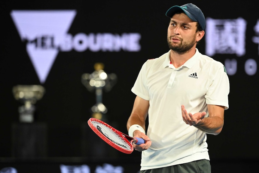 Aslan Karatsev stands and looks confused during an Australian Open tennis match against Novak Djokovic.