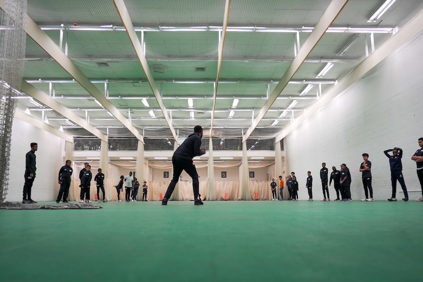 Children play cricket during a practice session at an indoor venue.