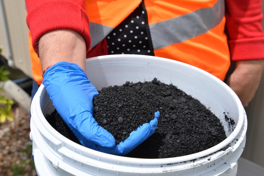 A person holding a bucket of a black gritty substance