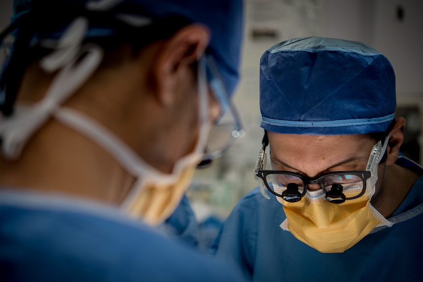 Two people in an operating theatre look over a patient.