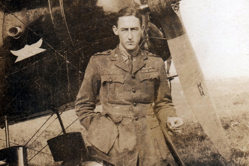 Young man in a WWI military uniform stands in front of a plane towards the end of war, circa 1918.