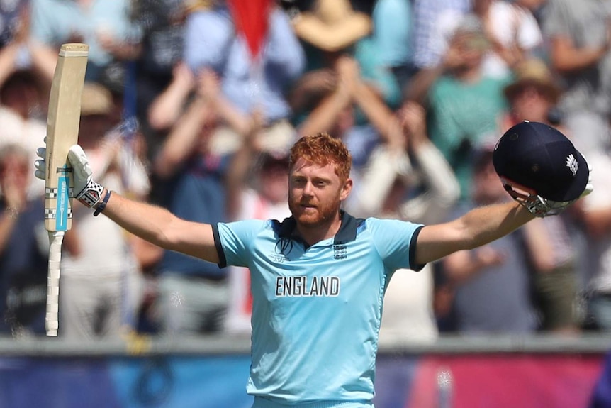 Jonny Bairstow holds his bat in one hand and helmet in the other as he spreads his arms in celebration.