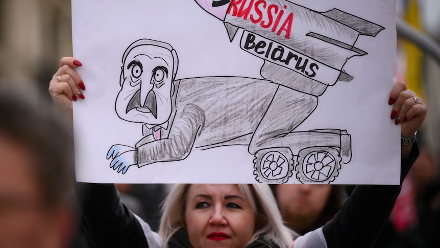 A protester holds a sign protesting against Belarus's support for Russia in the war against Ukraine.
