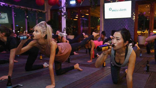 Women do yoga pose with beer in one hand
