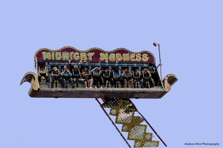A show ride in the shape of a couch called Midnight Madness spinning in the sky with a group of people on it having fun.