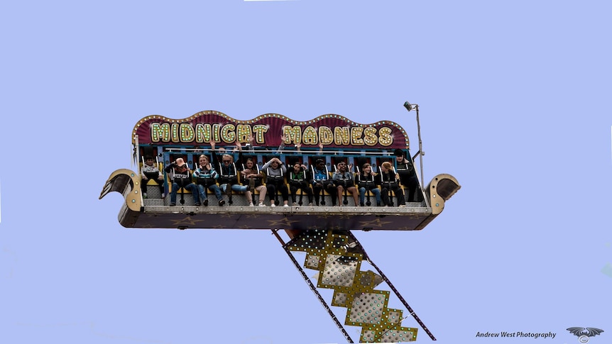 A show ride in the shape of a couch called Midnight Madness spinning in the sky with a group of people on it having fun.