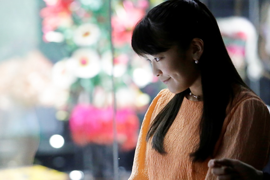 A woman with black hair looks down with the lights of the city behind her.