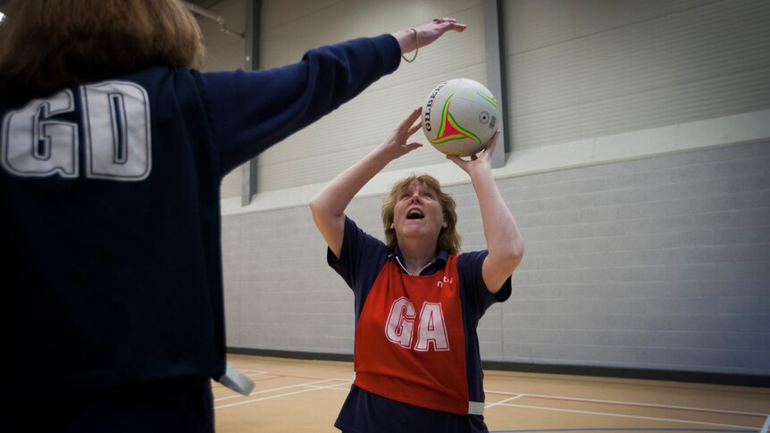 A woman wearing a goal attack bib shoots for goal on a netball court