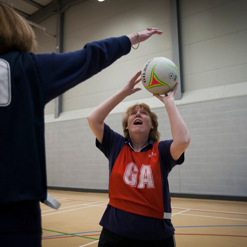 A woman wearing a goal attack bib shoots for goal on a netball court
