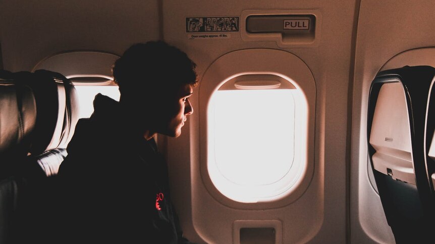 A man sits next to a window in the main cabin of a airplane.