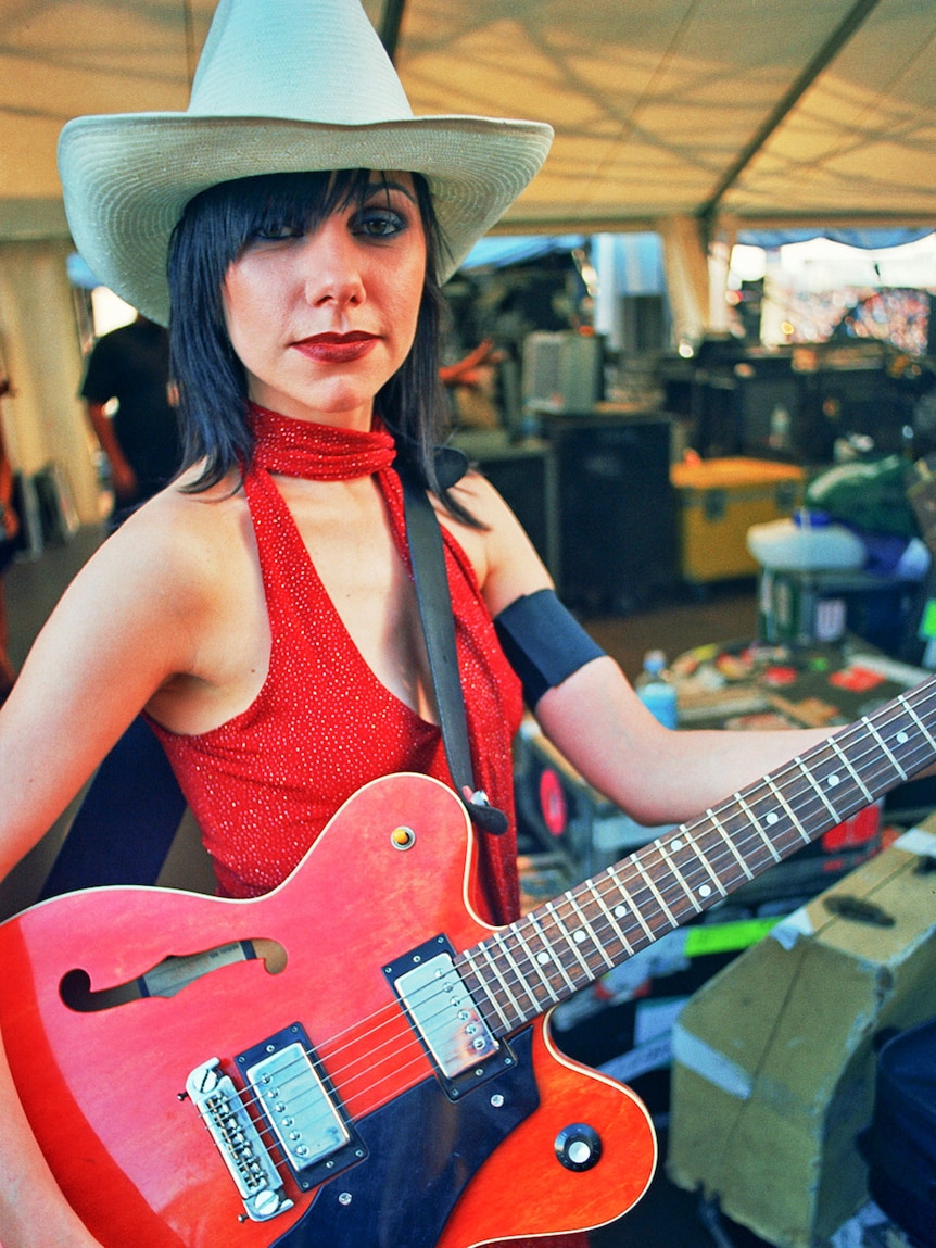 PJ Harvey wearing a wide-brim hat and red dress, holding a red Gretsch guitar