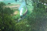 A steam train travels along a wooden rail bridge that is raised above the green fields around it.