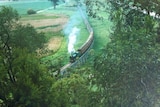 A steam train travels along a wooden rail bridge that is raised above the green fields around it.