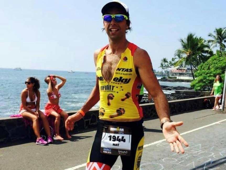 An Indigenous man wearing athletic gear jogs while competing in a triathlon.