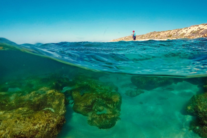 A close-up of ocean water, with a woman standing in water in the distance.