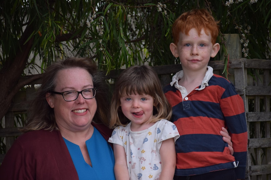 Woman with a boy and girl smiling, one has red hair and wearing red/blue jumper. The other a brown bob with tongue stuck out.