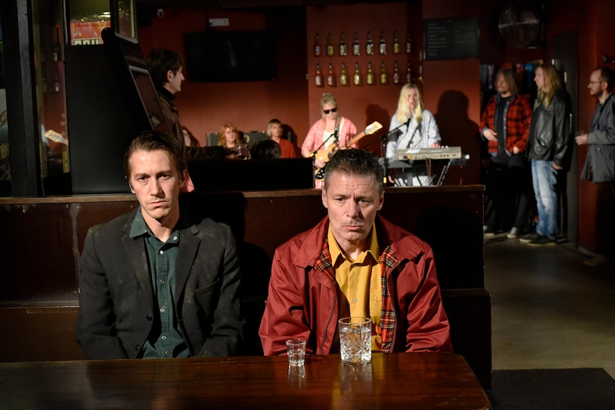 A film still of Jussi Vatanen and Janne Hyytiäinen, sitting side by side in a bar. They both look miserable.