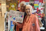 Two women stand together, holding a sign which reads old and bold deserve gold.