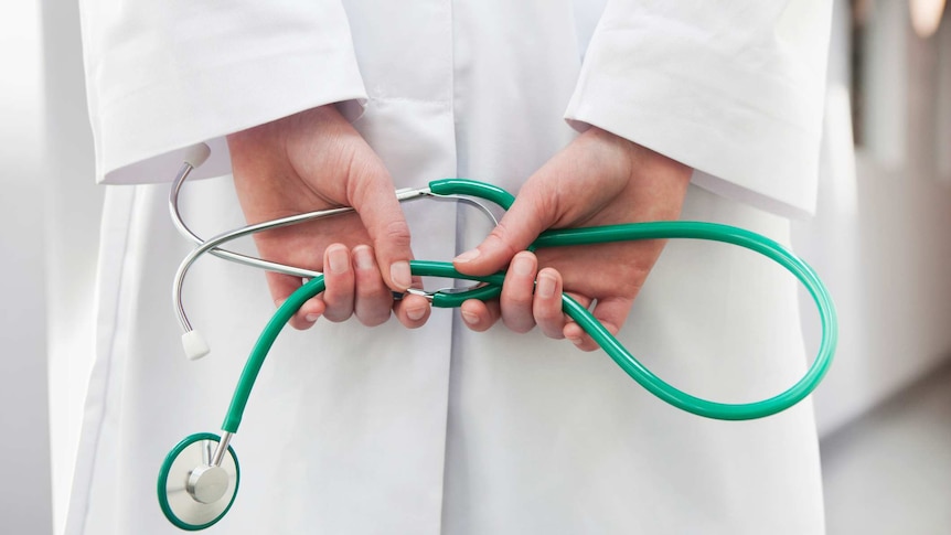 Closeup of female doctor in white lab coat with hands behind back holding green stethoscope