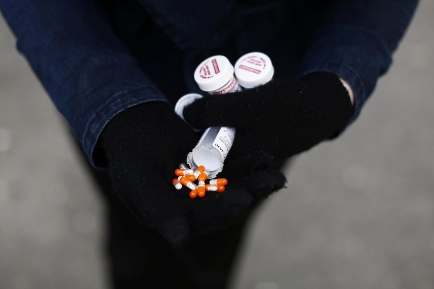 A pair of gloved hands holding pills and pill containers 