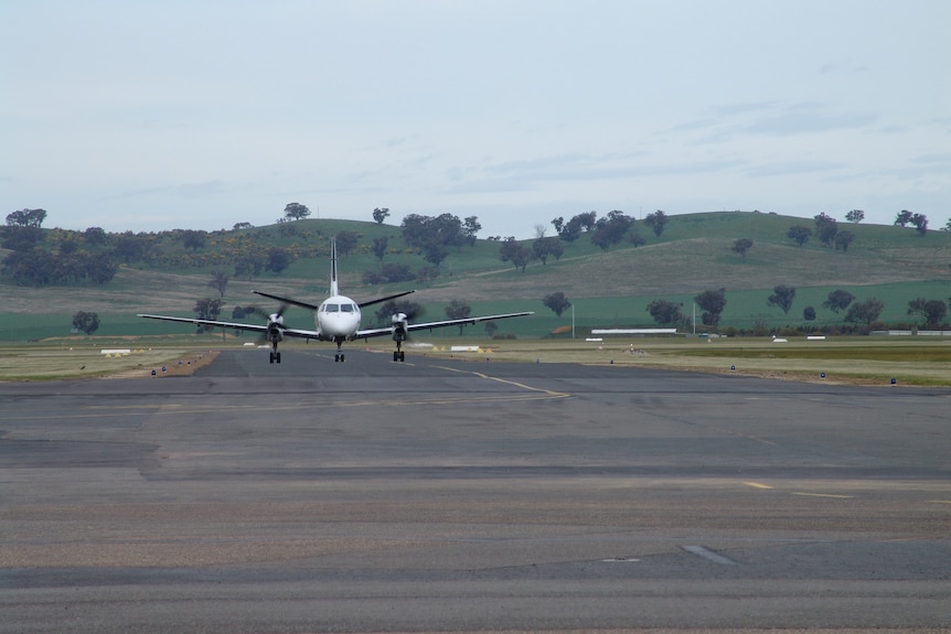 A small plan about the land on a runway with rolling grassy hill behind