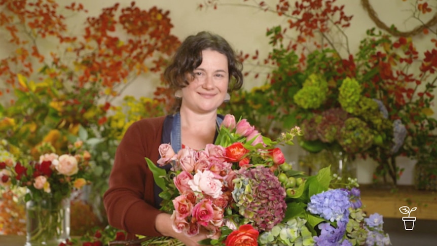 Woman surrounded by cut flowers holding large bouquet