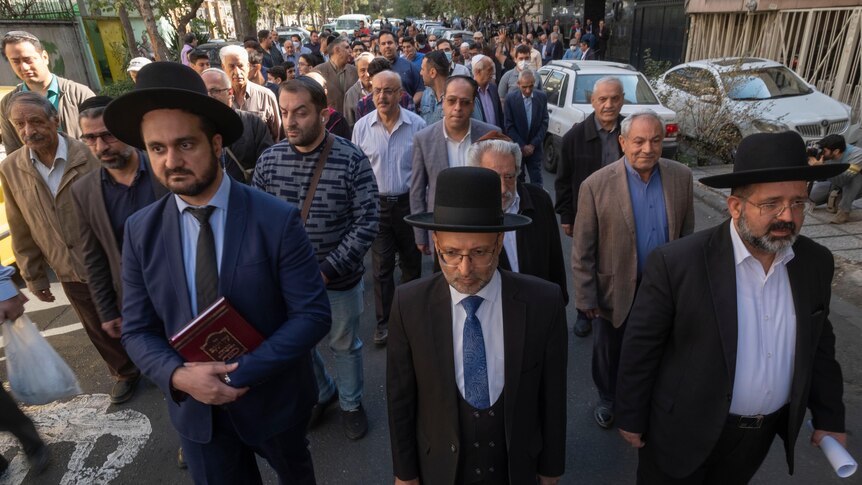 A group of men in traditional Jewish hats march in a Tehran street