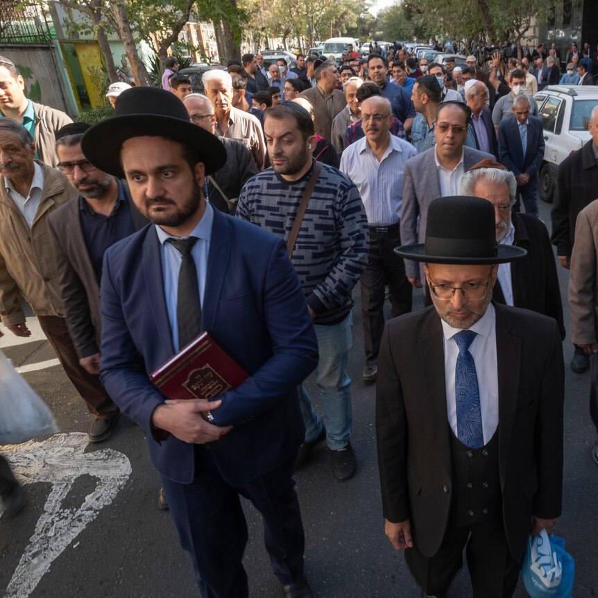 A group of men in traditional Jewish hats march in a Tehran street