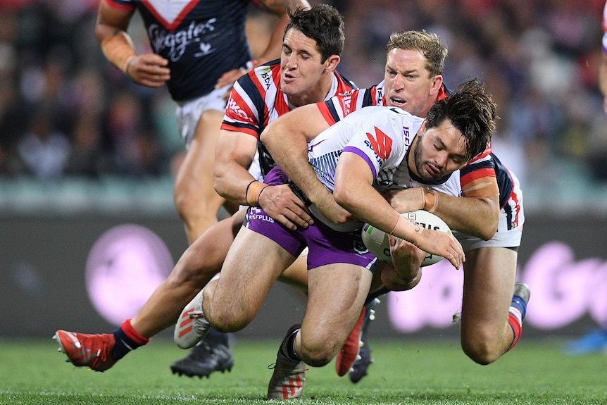 Melbourne Storm player Brandon Smith getting tackled by two Sydney Roosters players
