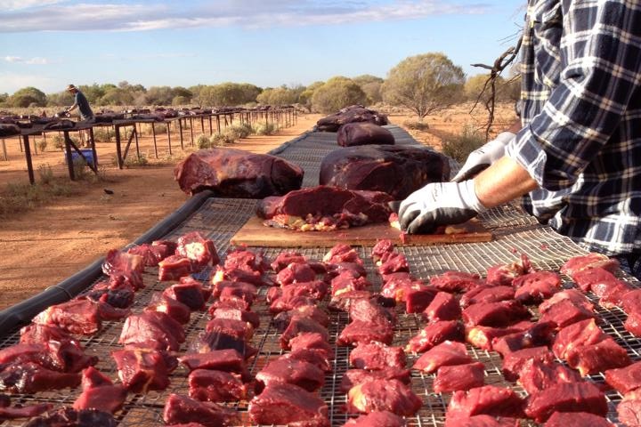 A pastoralist cuts up chunks of horse meat to make poison baits for wild dogs.