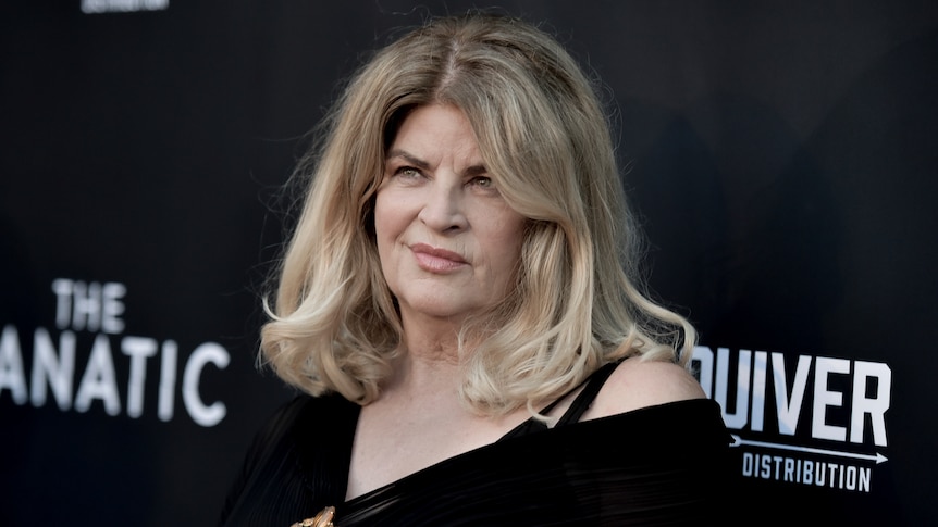 Kirstie Alley in front of a black board on a red carpet. 