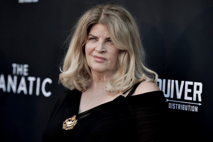 Kirstie Alley in front of a black board on a red carpet. 