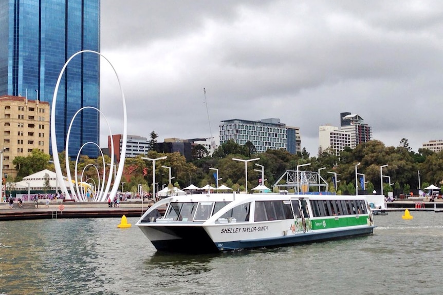 A Transperth ferry sails away from the Elizabeth Quay jetty with the Perth city skyline in the background.