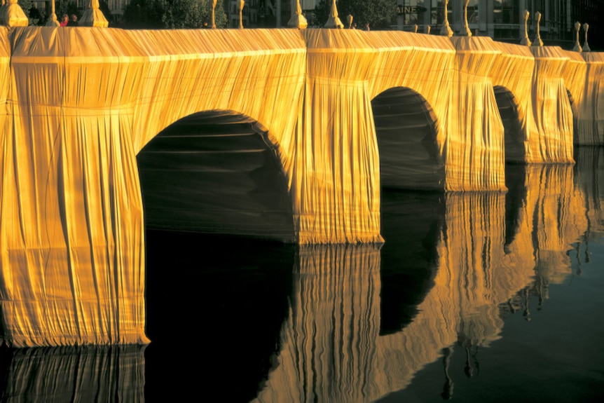 Yellow fabric wrapped around the iconic bridge reflects in the water 