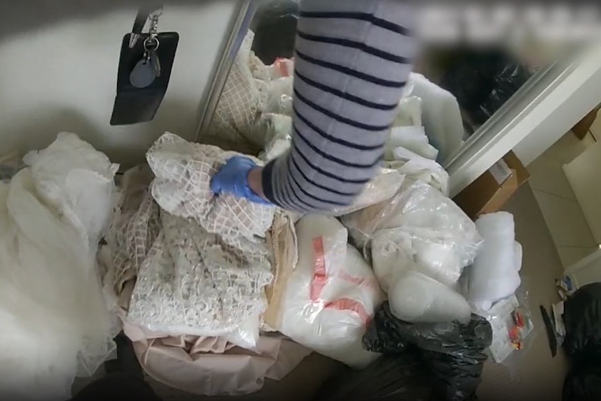 arm of detective sifting through pile of wedding dresses on floor