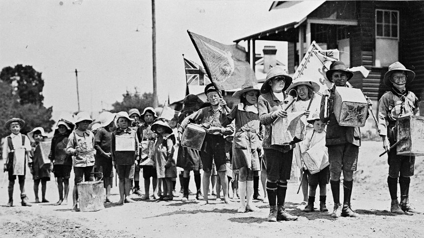 An Armistice Day parade by the children of the Duntroon public school. They are holding flags and boxes.