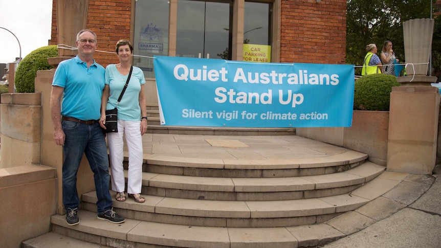 Rod and Margot Cunich standing on the steps in front of Dave Sharma's electoral office with a Quiet Australians Stand Up sign