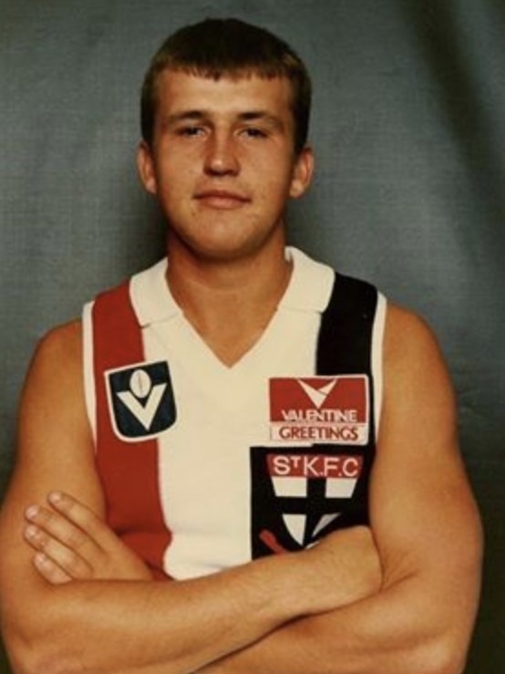 A man in a St Kilda jersey crosses his arms and smiles.