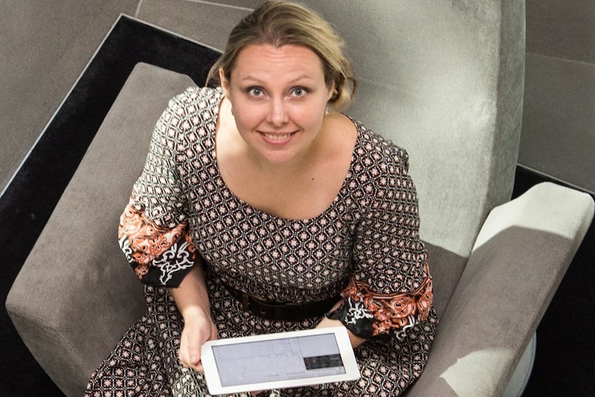 A woman holding an iPad sits in a chair.