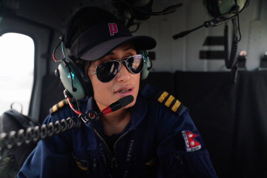 A woman sits in the cockpit of helicopter wearing aviator sunglasses