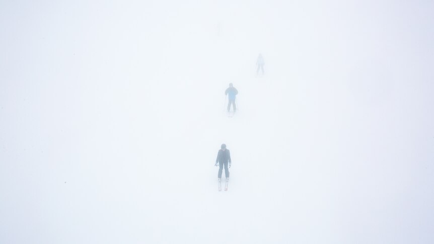 Skiers emerge out of the mist.