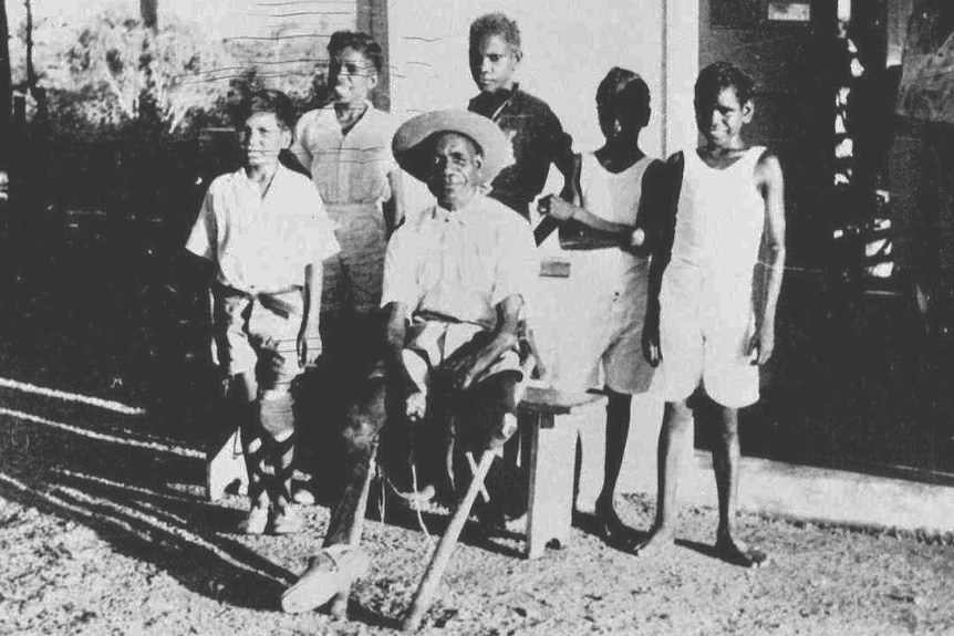 Man with wooden legs with children at the Channel Island leper colony.