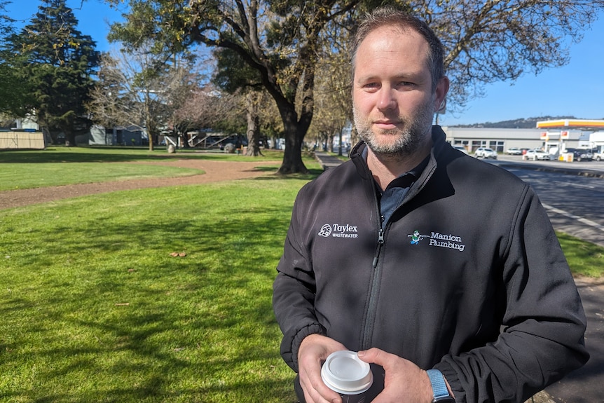 A man stands by the side of a road with a cup of coffee.