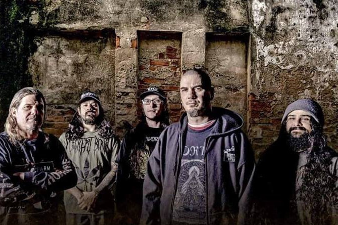 Moody, dimly lit shot of Philip Anselmo with his bandmates from The Illegals standing in front of a brick wall.