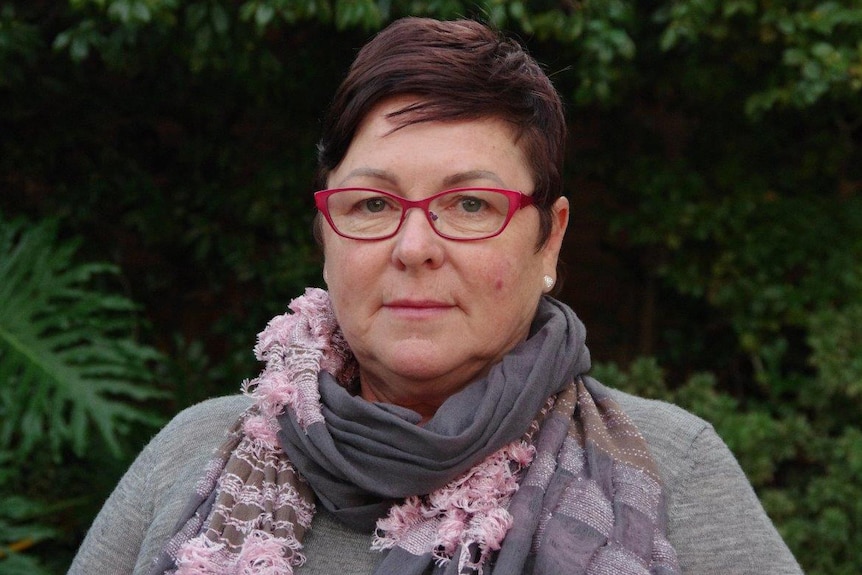 Lisa Baker stares at the camera wearing a grey scarf and pink glasses.